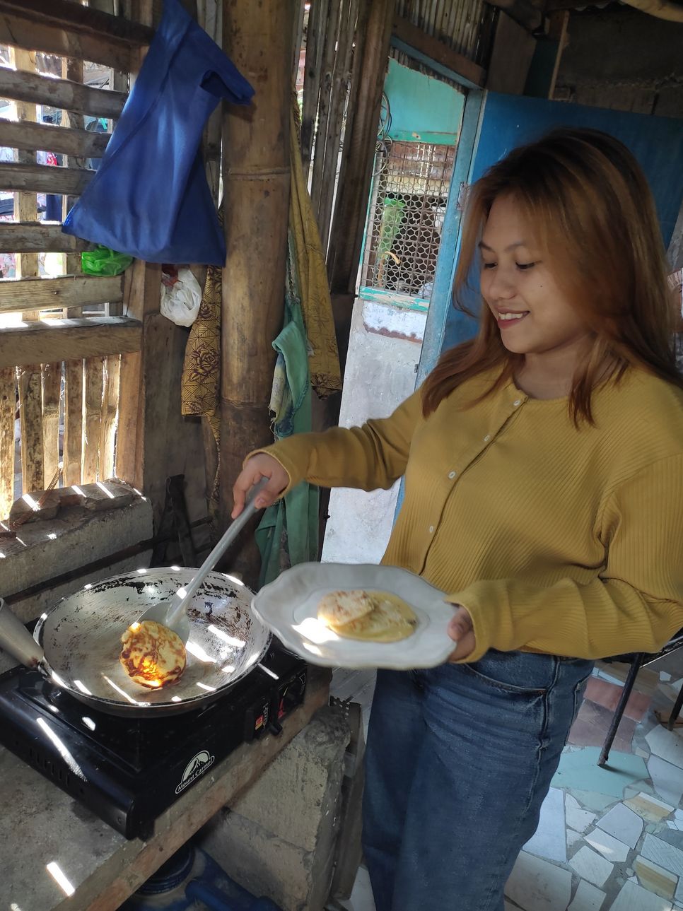 Eine junge Frau steht, mit einem Teller und einem Pfannenwender in der Hand, vor dem Herd und kocht.