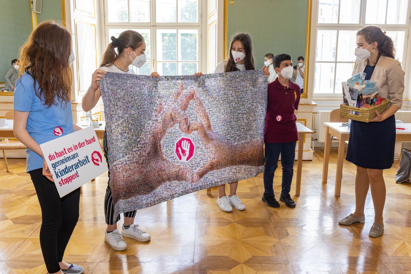Kinder der Aktion Kinderarbeit stoppen überreichen der Bundesministerin Alma Zadić das Transparent des Mosaik aus den symbolischen Fotos der Hände gegen Kinderarbeit 