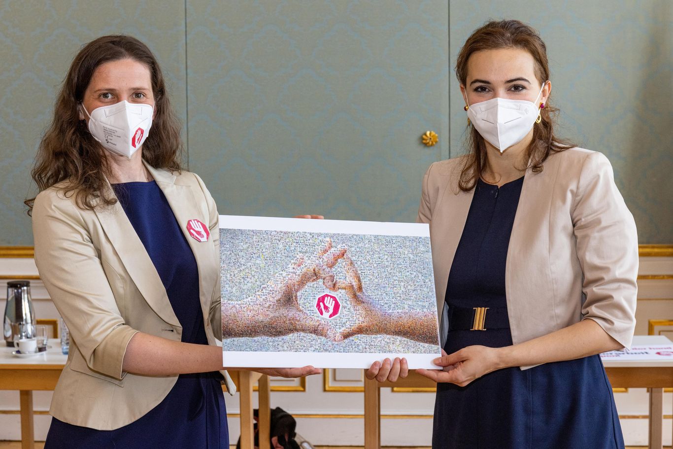 Eine Vertreterin der Aktion Kinderarbeit stoppen hält zusammen mit Bundesministerin Alma Zadić das Mosaik aus den symbolischen Fotos der Hände gegen Kinderarbeit 