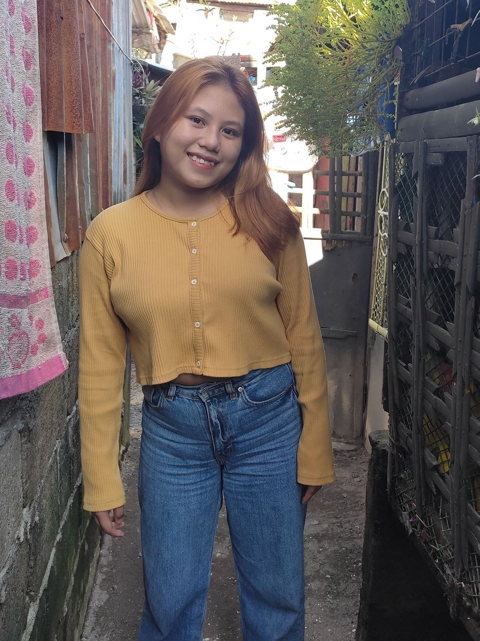 Eine junge Frau in Jeans und einem gelben Pullover lächelt.