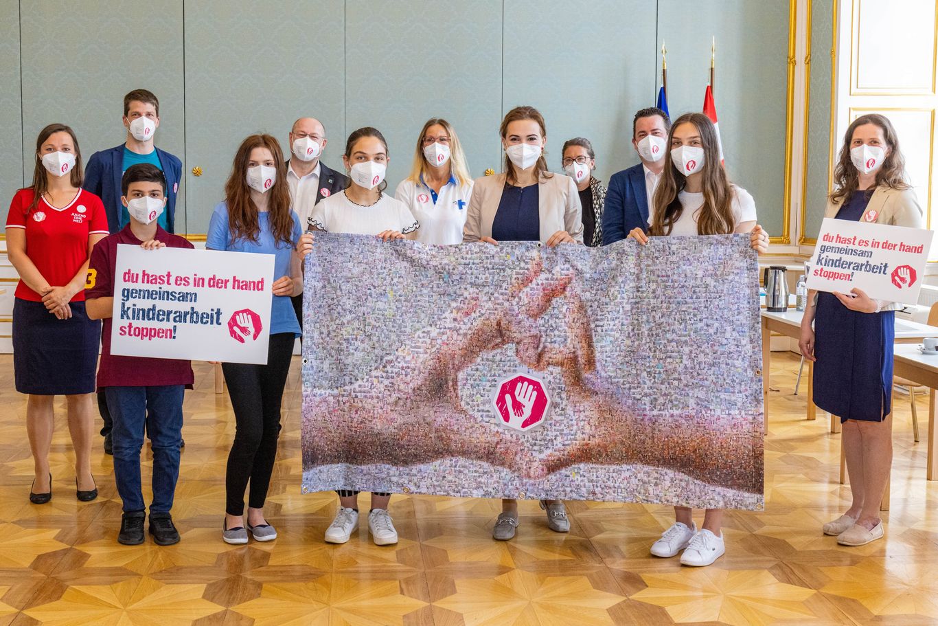 Kinder der Aktion Kinderarbeit stoppen halten mit Bundesministerin Alma Zadić das Mosaik aus den symbolischen Fotos der Hände gegen Kinderarbeit 